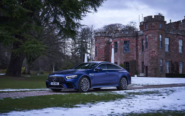 A blue Mercedes-Benz AMG GT parked on a snowy lawn in front of a historic stone castle, captured in 4K Ultra HD for a PC desktop wallpaper.
