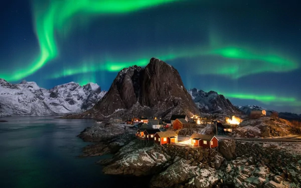 HD desktop wallpaper showcasing the vibrant aurora borealis over snowy mountains and a coastal village in Lofoten, Earth, captured through stunning photography.