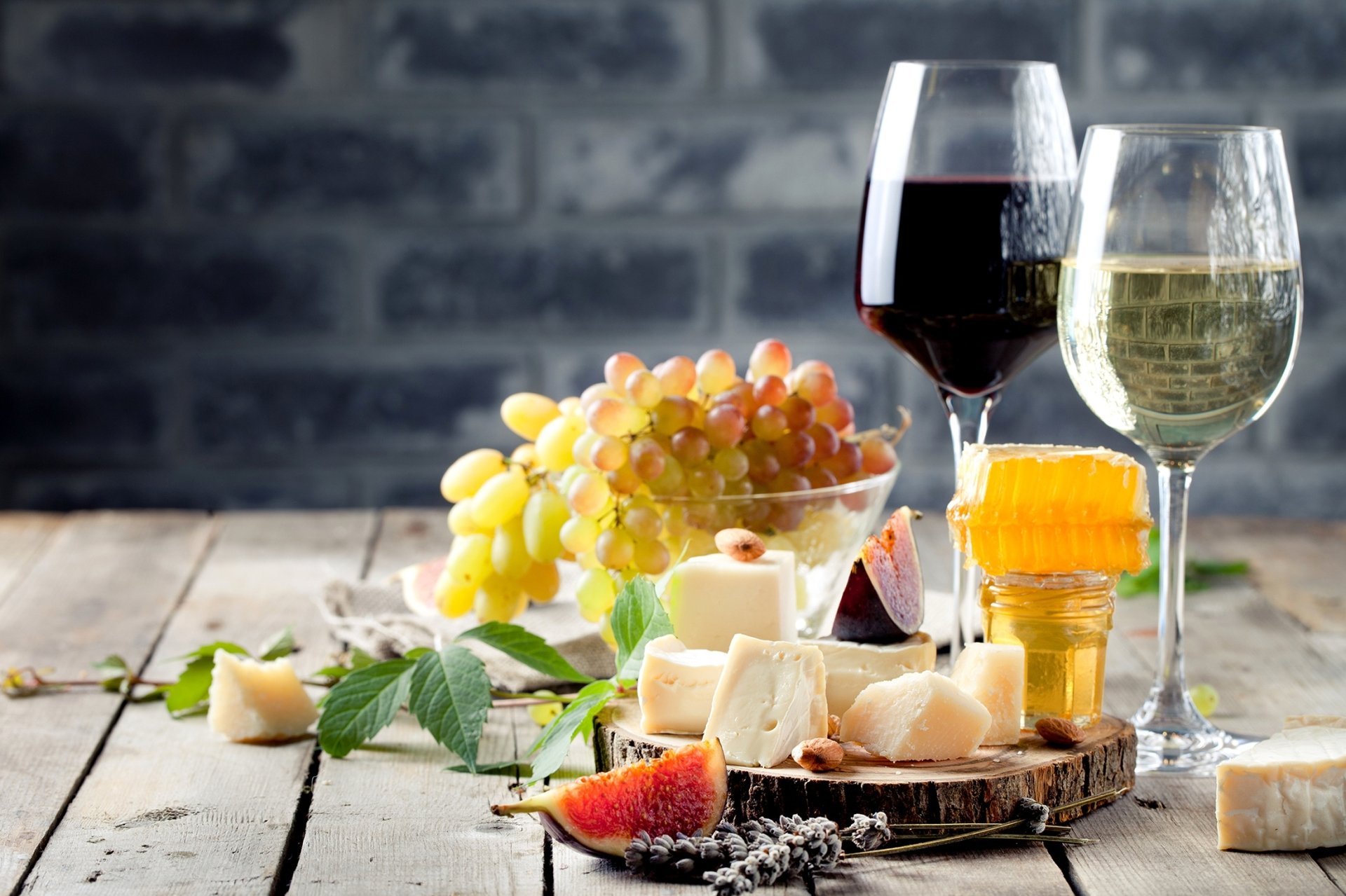 HD PC desktop wallpaper and background: still-life of red and white wine glasses, grapes, assorted cheeses, figs and crackers on a rustic wooden board.