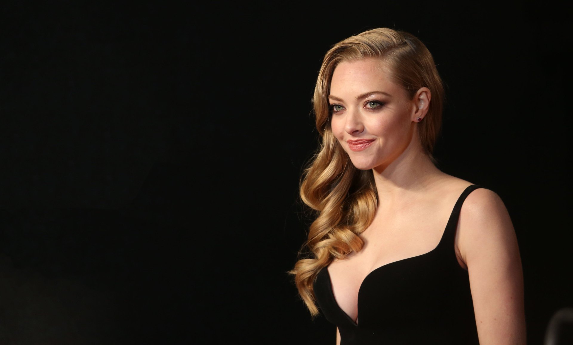 Blonde American actress Amanda Seyfried smiles confidently against a dark background in this 4K Ultra HD desktop wallpaper and background image.